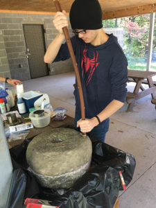 Appalachian Male Initiative student learns to grind corn on old-fashion grinding stone.