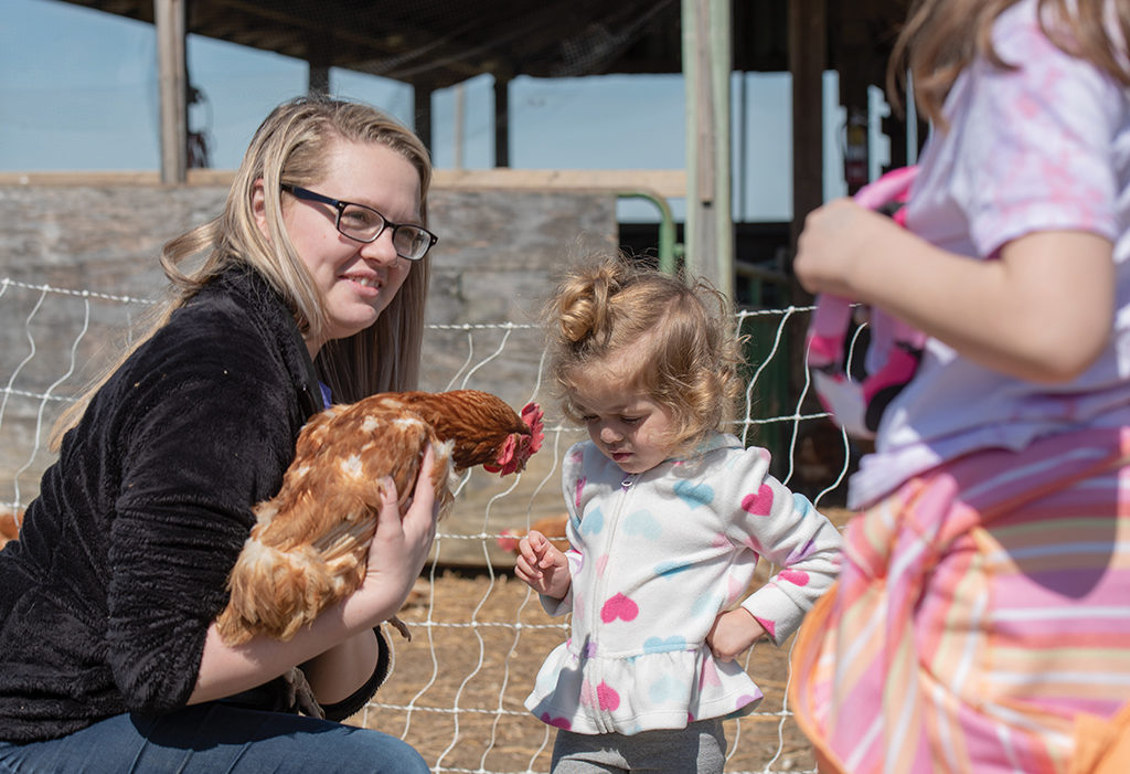 Jessie Adams holds rooster up for little girl to see