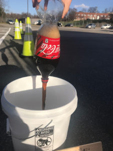 One of the students prepares a bottle of Coca-Cola that will later be poured onto the pavement.