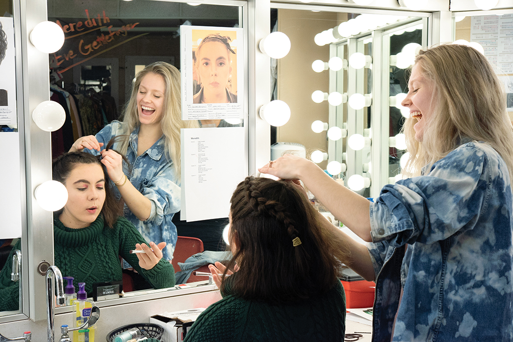 Students back stage doing hair and makeup for a theater production