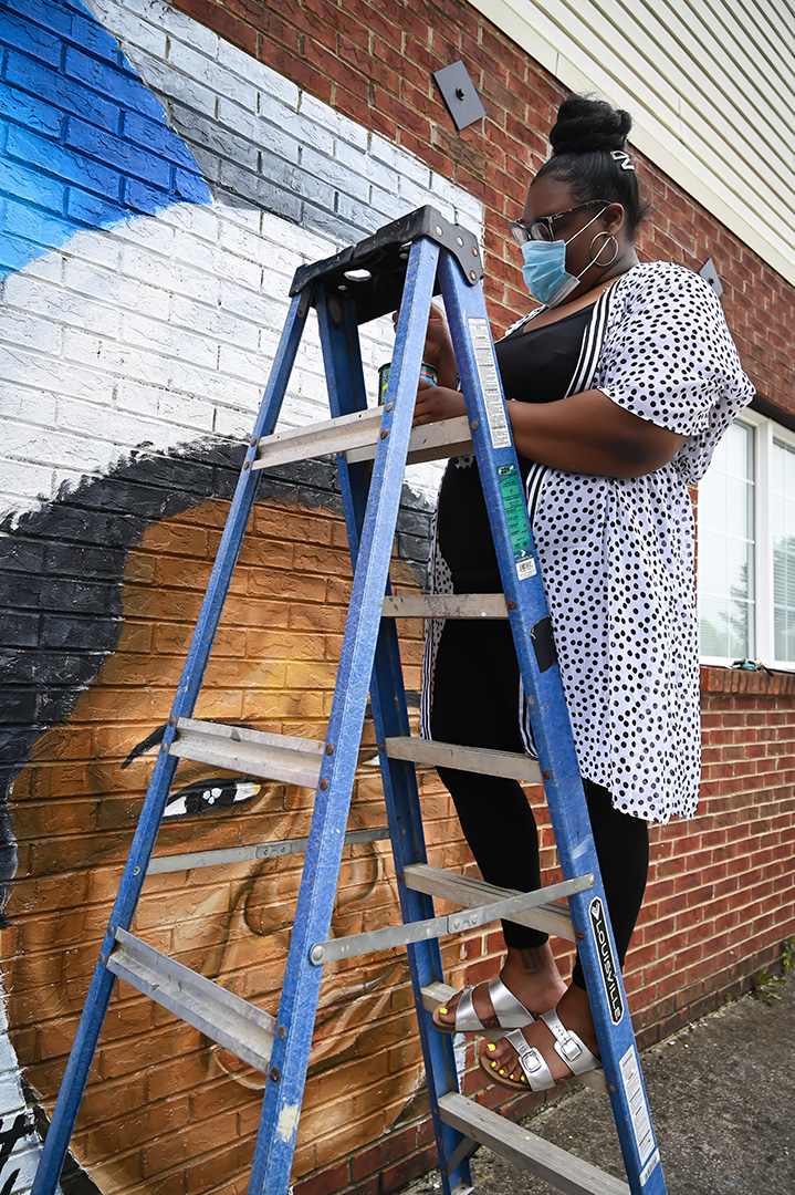 Artist applying a seal to the mural from a ladder