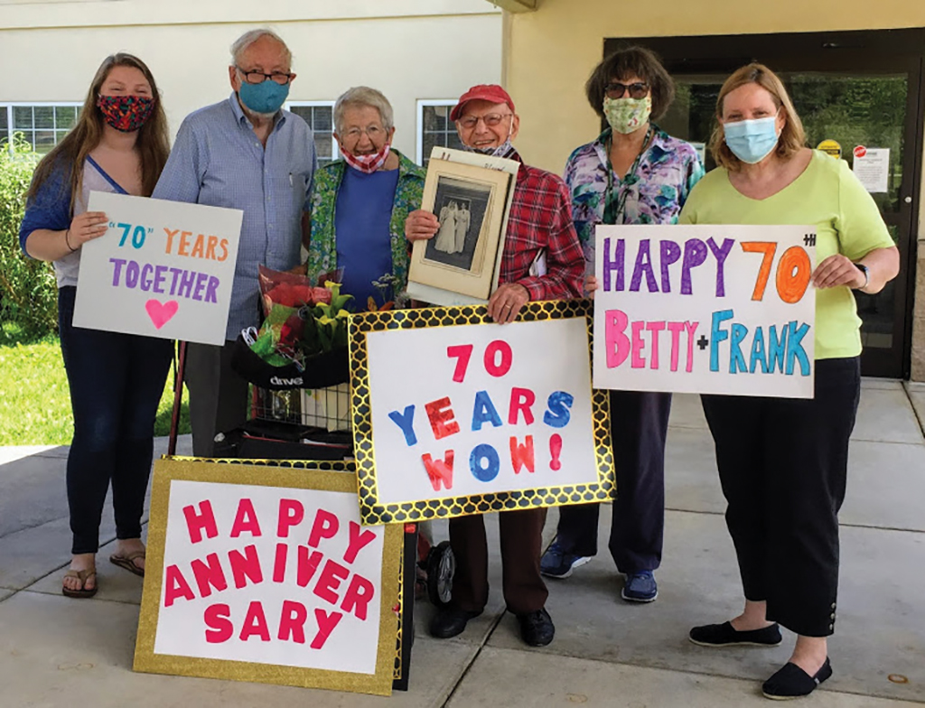 Franklin and Betty Parker stand outside of their community building with signs celebrating their 70th anniversary
