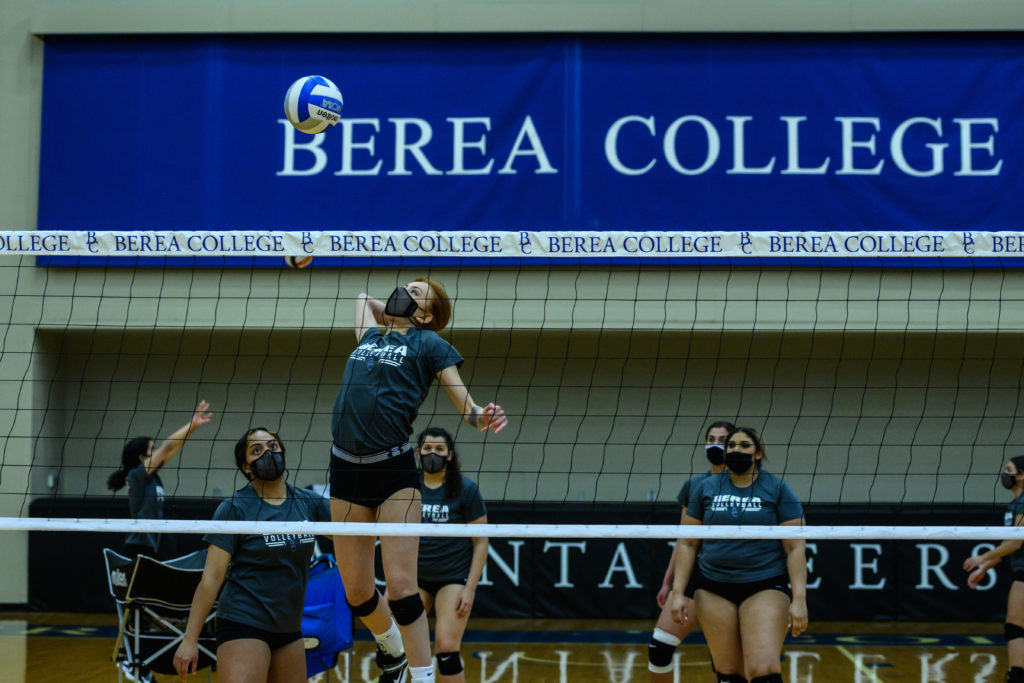 Volleyball player jumping in the air to hit a ball over the net in Seabury arena