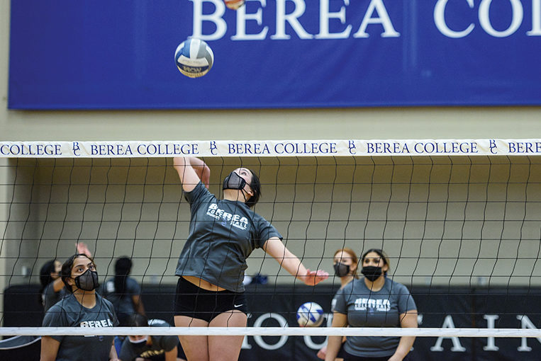 Volleyball player jumping in the air to hit a ball over the net in Seabury arena