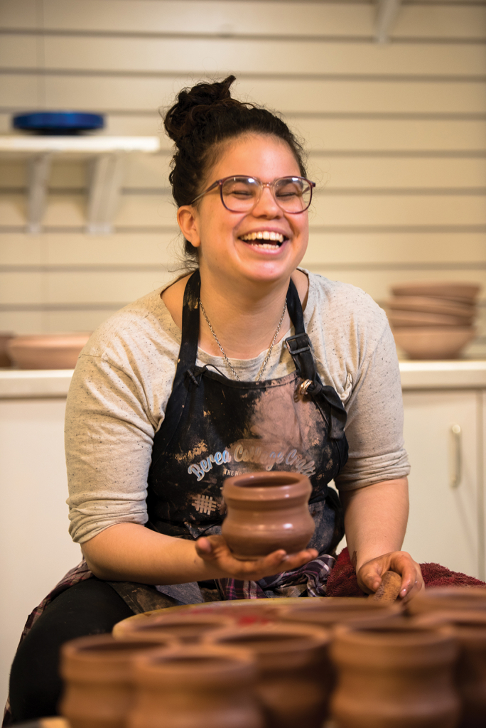 Student laughs while crafting a clay pot at a pottery wheel