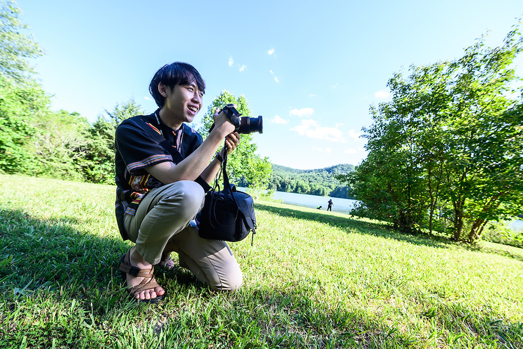 Student kneeling to take a photograph in the grass