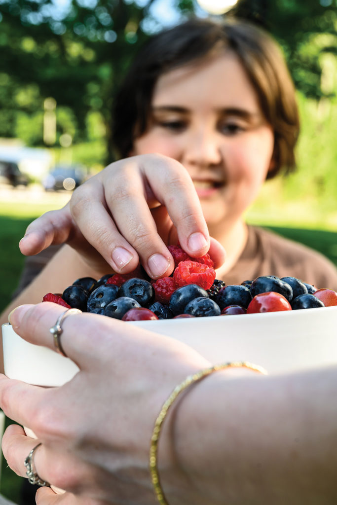 A bowl of strawberries, blueberries and blackberries with a little boy choosing berries to eat