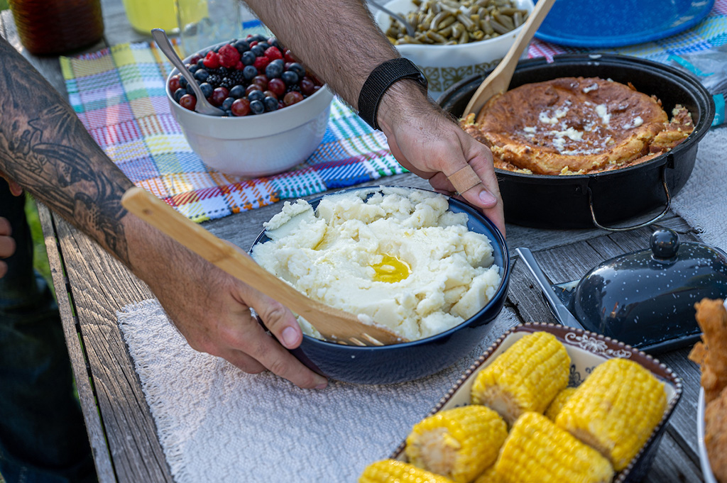 Man placing a bowl of mashed potatoes on a farm table filled with food