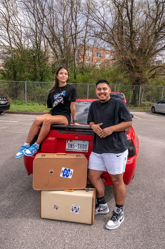 Portrait of Diana and Alexis sitting on a red car with two suitcases