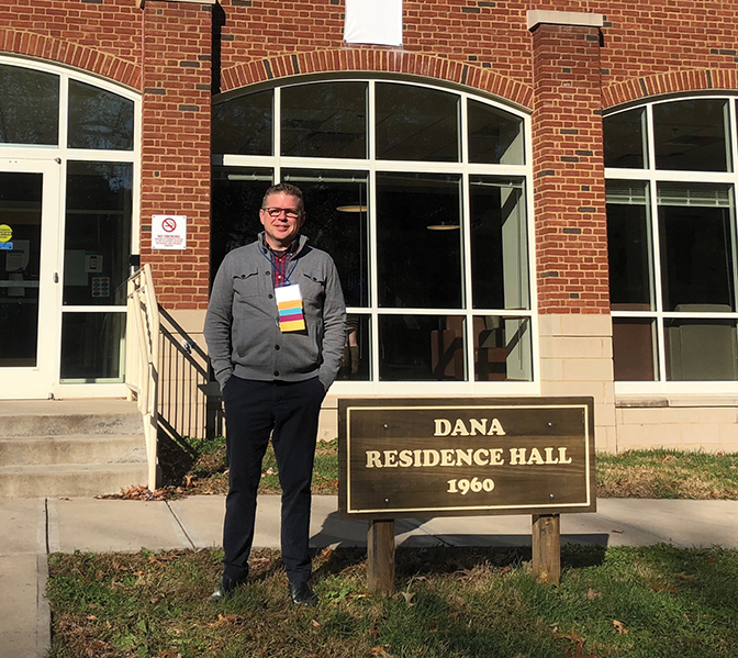 Photo of Dr. Adam Howard standing next to the Dana Residence Hall sign