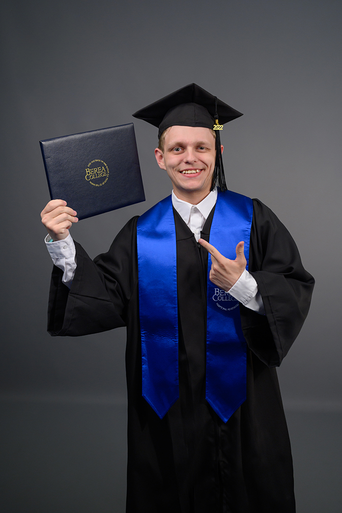 Graduation photograph of Dustin Copper hoolding his degree folder.