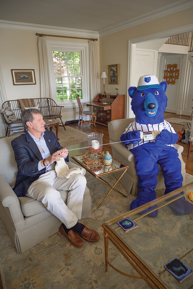 Lyle Roelofs sits in his home with mascot Blue knitting