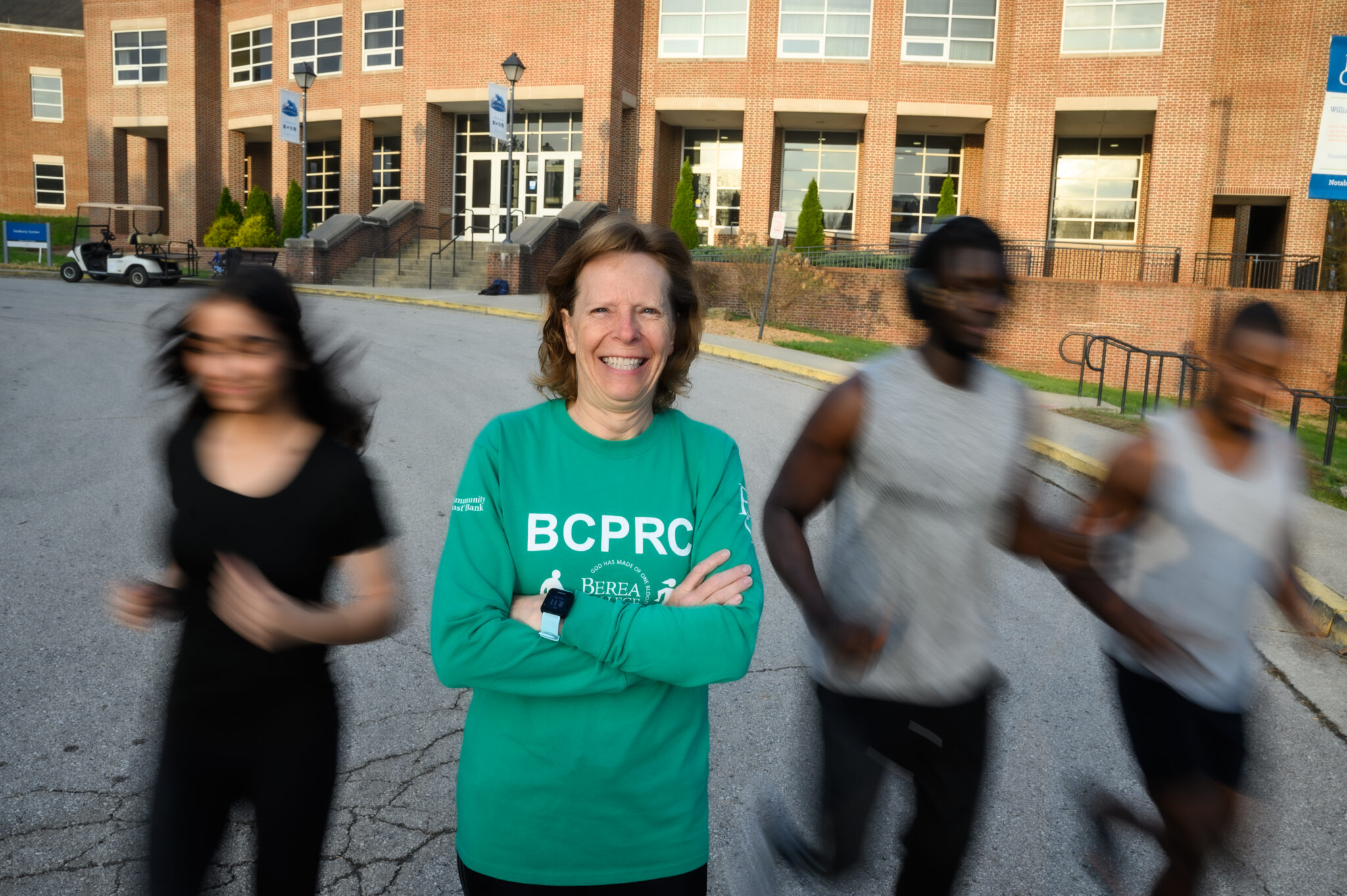 photo of Teri Thesing in a President's Run/Walk Club shirt with students running behind her in blurred motion