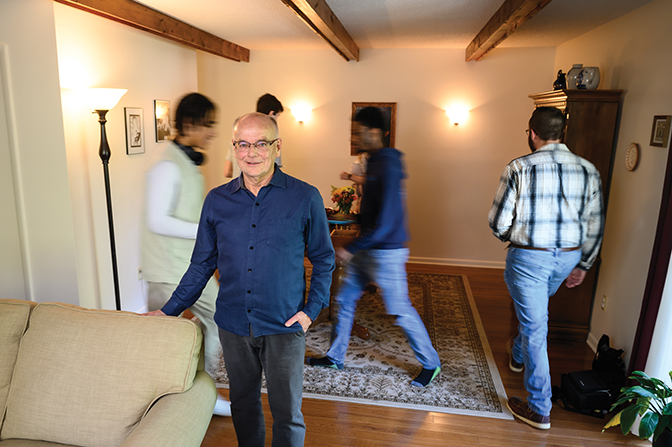 Dr. Steve Gowler stands in his living room while students get food behind him.