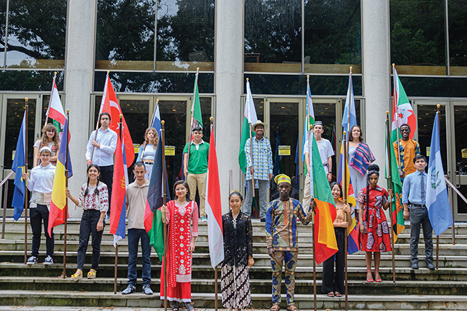 Group of international students stand with all their countries' flags on the front steps of Hutchins Library