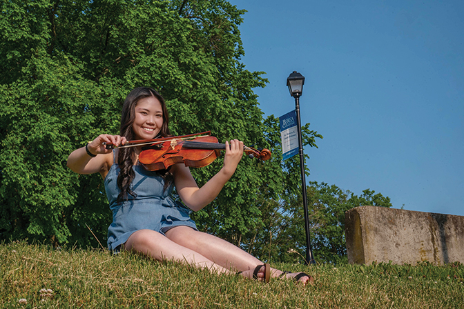 Kimberly '26 plays the fiddle sitting in the grass near the MAC building