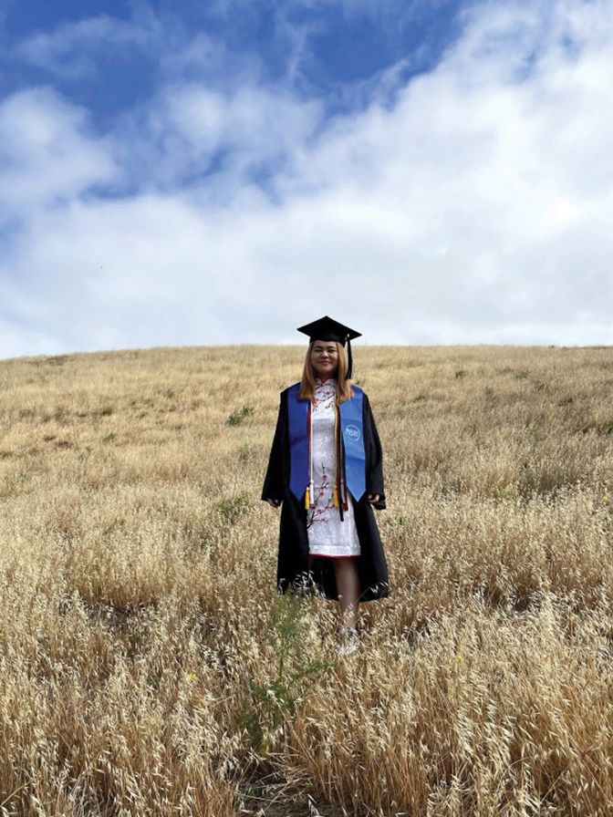 Portrait of Michelle Atkinson standing with her cap and gown on in a field