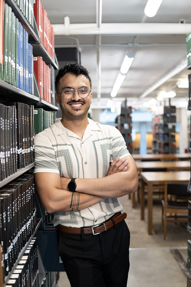 Portrait of Yogesh Budhathoki '22 leaning against a stack of books in a library