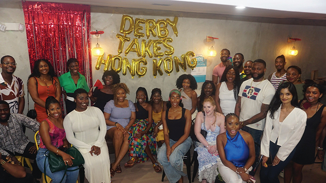 Group of people huddled around large gold letters that read "Derby Takes Hong Kong"