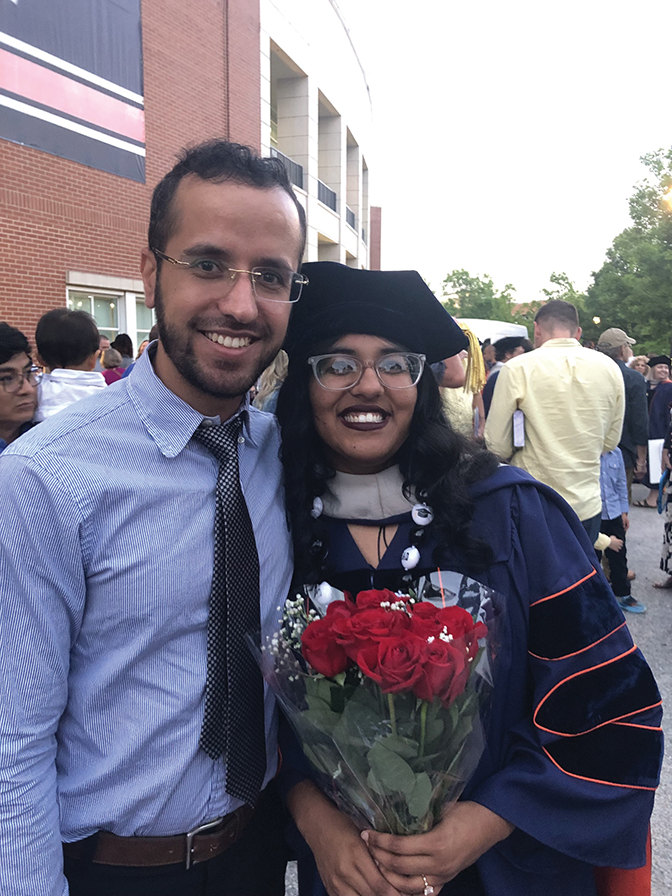 Portrait of Sara Holly in cap and gown standing with a gentleman