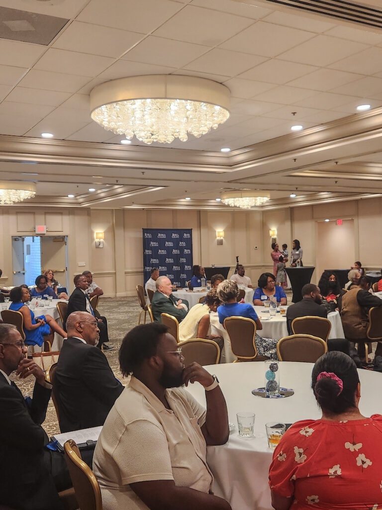Greenville alumni sit at tables and listen to a presentation.