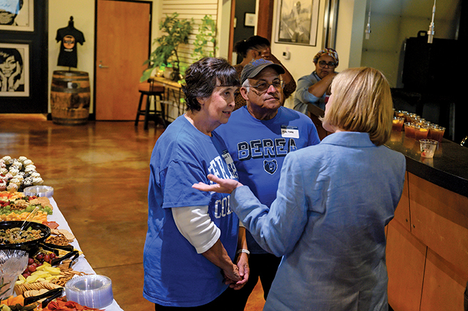 Two alumni listening to President Cheryl Nixon talk to them