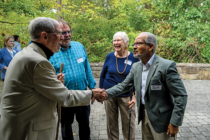 Two men shaking hands with two other laughing in the background