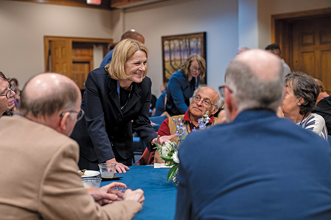 President Cheryl Nixon leans over a table to talk with a group of alumni