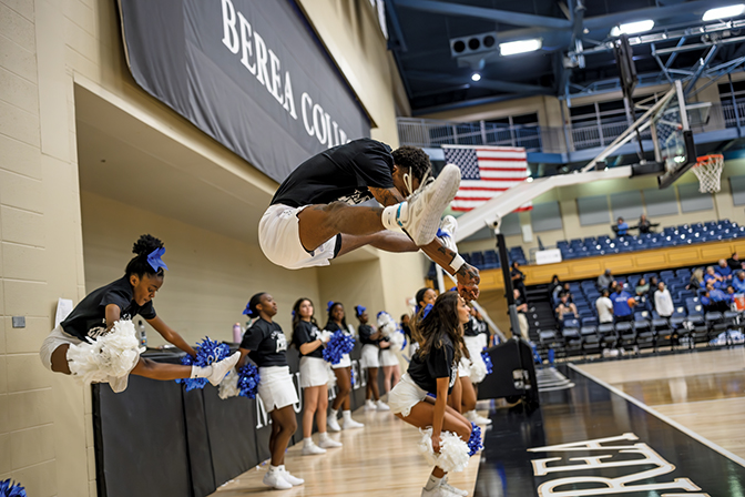 Two cheerleaders in the air mid-jump on the sideline of a basketball game