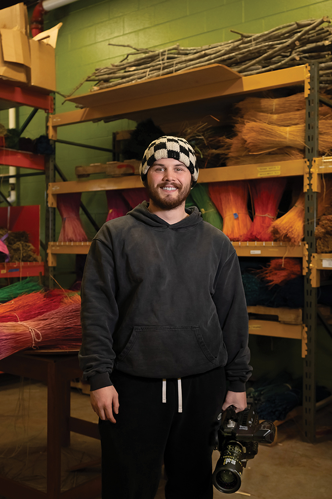 Portrait of Sean Hall in the Student Craft broommaking studio holding a video camera