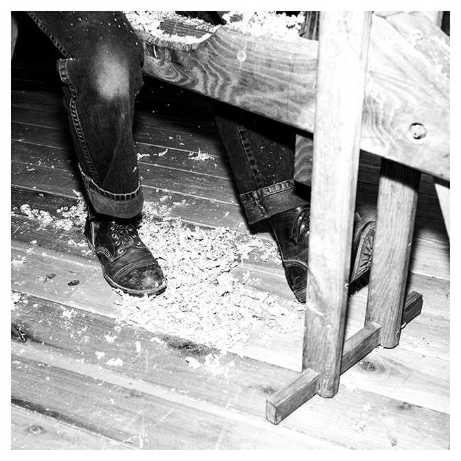 black and white image of feet covered in saw dust under a machine that carves wood