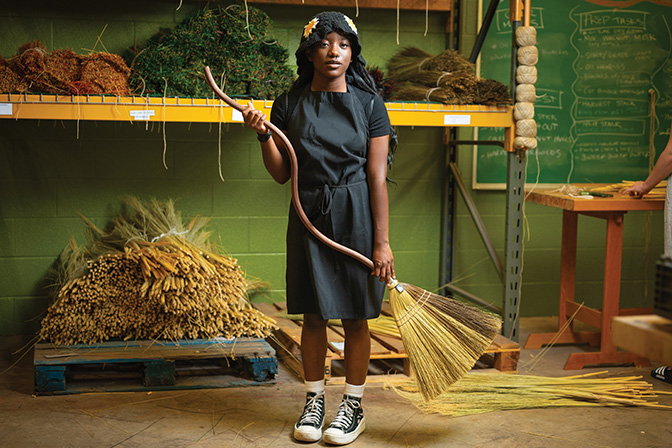 Photo of a girl in a dress holding curvy handle Appalachian broom in Student Craft