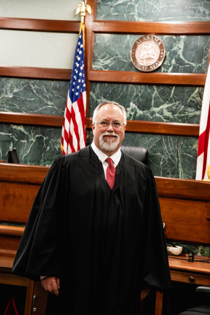 Judge John Graham standing inside a courtroom with two flags