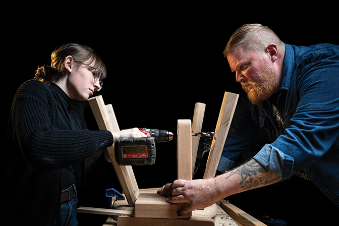 Photo of a student and staff member screwing the legs onto a stool