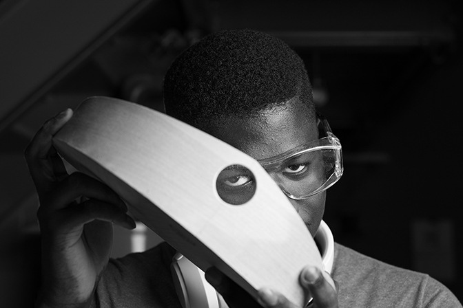 Black and white image of a young man looking the hole of a piece of wood in Student Craft