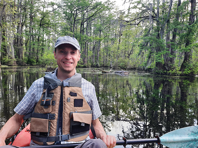 Photo of Perrin de Jong in a boat in a body of water surrounded by trees.