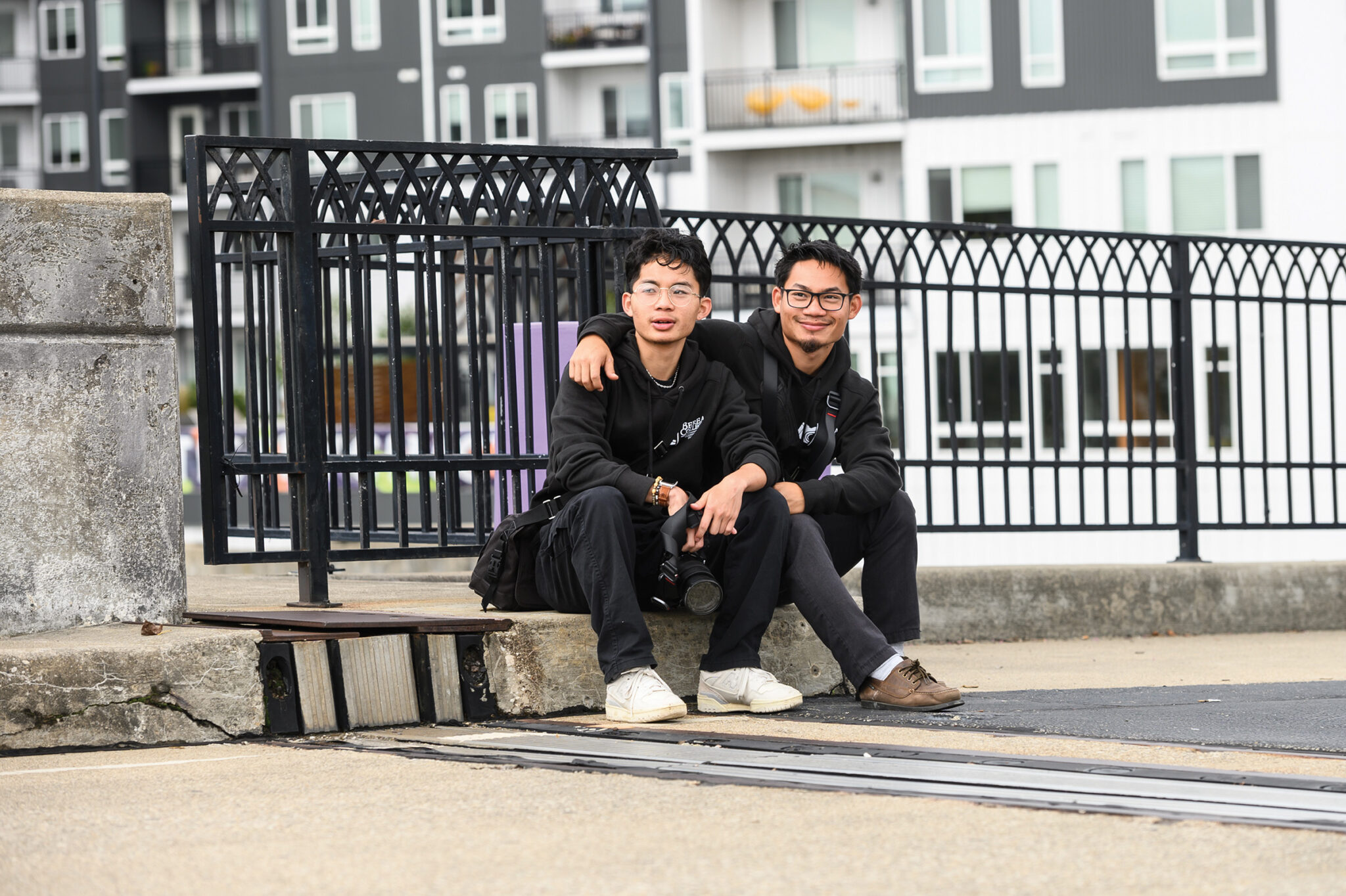 Ehku and Nay sit on the curb on a bridge during a photography student training in Cincinnati.