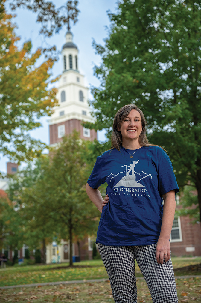 Denessa McPherson '05 is wearing a blue shirt and is standing outside on campus. Draper is visible in the distance.