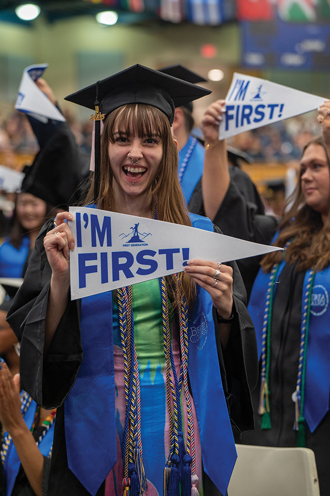 A graduate holds a pennant that reads, "I'm First!"