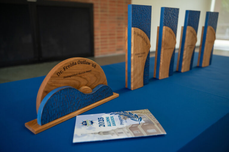 Image of four alumni awards lined up on a table with a blue tablecloth