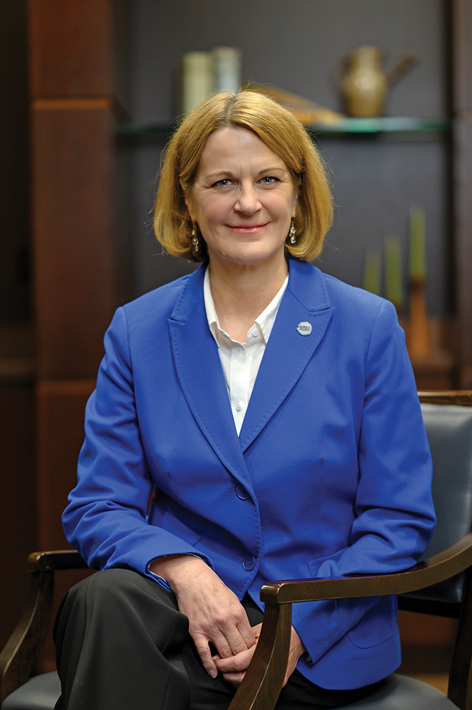 President Nixon sits in a chair wearing a white shirt, blue blazer, and black pants.