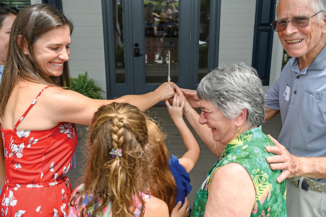 Photo of four people in the Best-Evans family preparing to cut the ribbon in front of the new Best-Evans house.