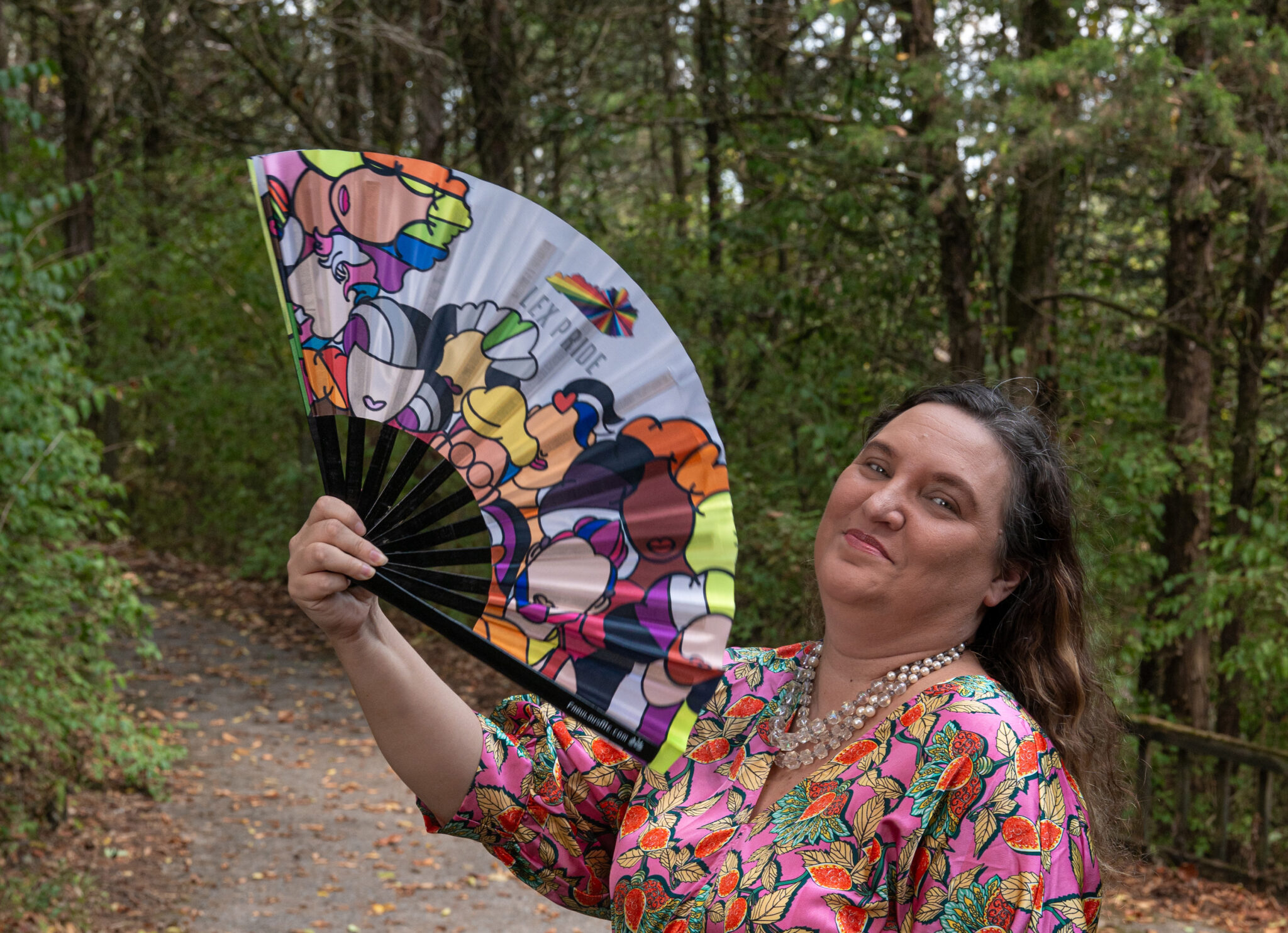 Transformative Spaces Melissa Benson stands on a path in the woods wearing a colorful dress and holding a colorful folding fan.