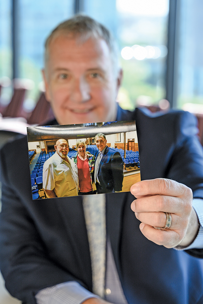 Mark Godsey holds a photo of himself with his father, Maurice Godsey ’60, and his sister Amy Alexander, taken on the stage of Phelps Stokes Chapel after his 2019 Berea convocation. Godsey, a former prosecutor, now directs the Ohio Innocence Project and has helped free 43 wrongfully convicted people. Photo by Crystal Wylie ’05