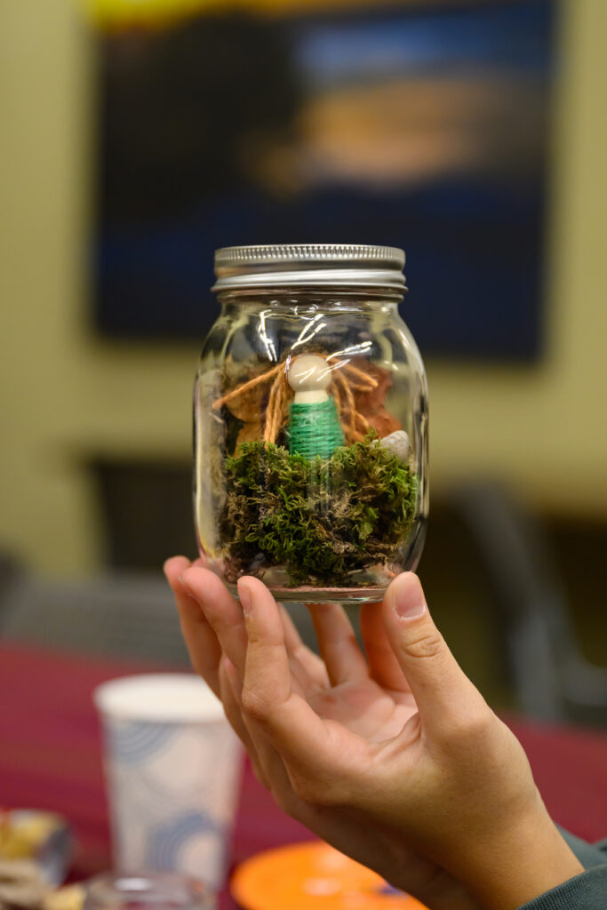 A student holding up an art piece made out of a jar.