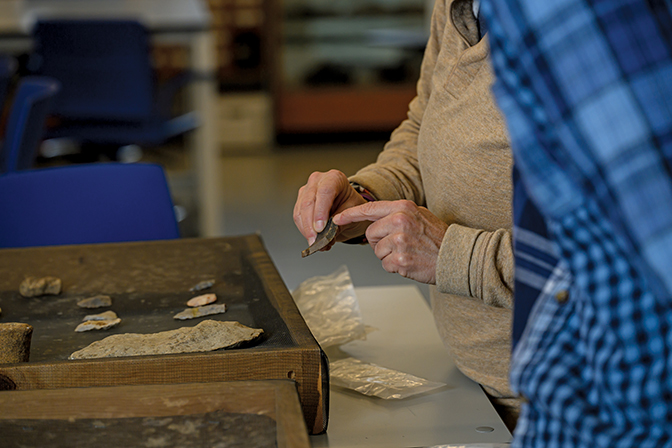 Close up image of hands pointing to an arrowhead artifact.