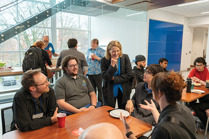 President Cheryl Nixon listens to several alumni talk around a table in the new CMIT building.