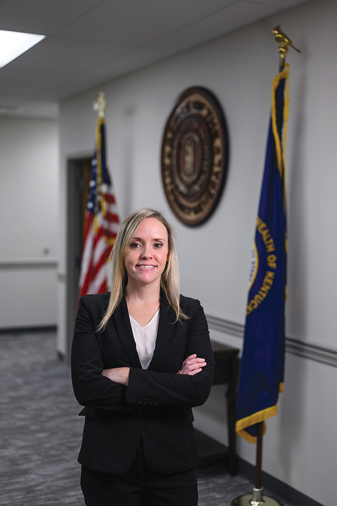 Portrait of Linsey Hogg with official flags and seal in the background.