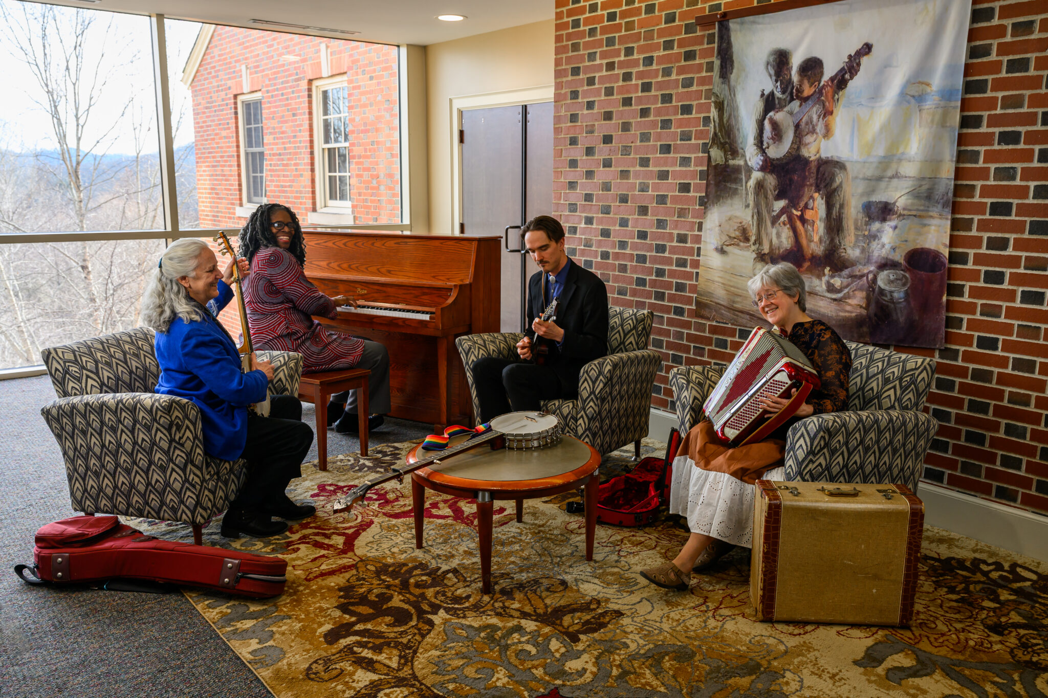 The Music of Other Appalachians Photo of four people sitting in a space with large windows all playing different instruments and laughing
