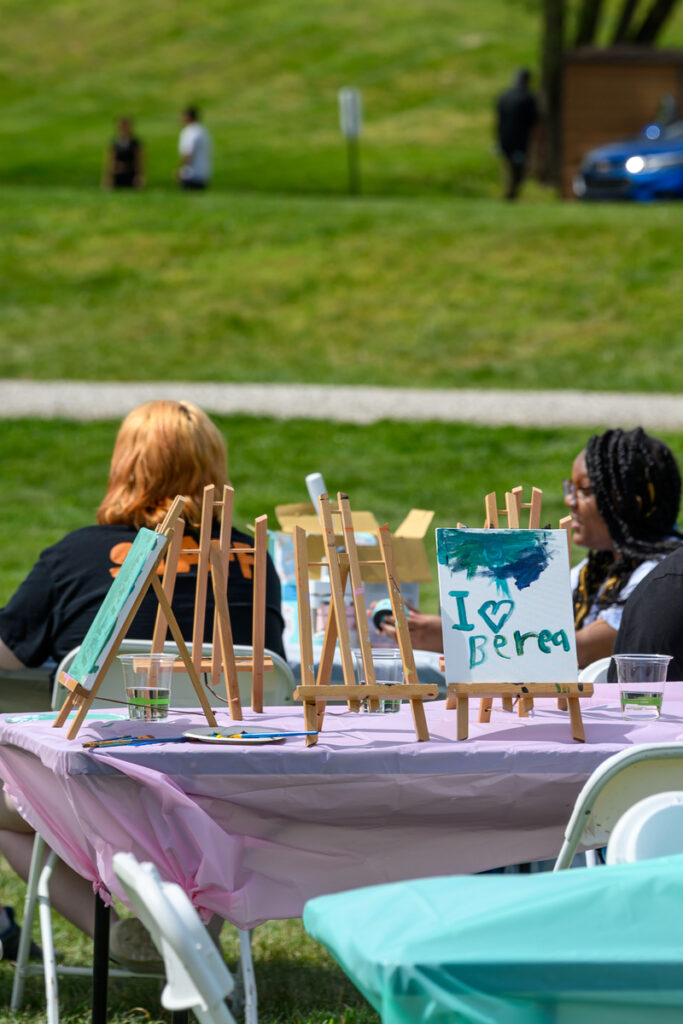 Two students sitting at a table in the background, with a painting that says I love Berea in the foreground